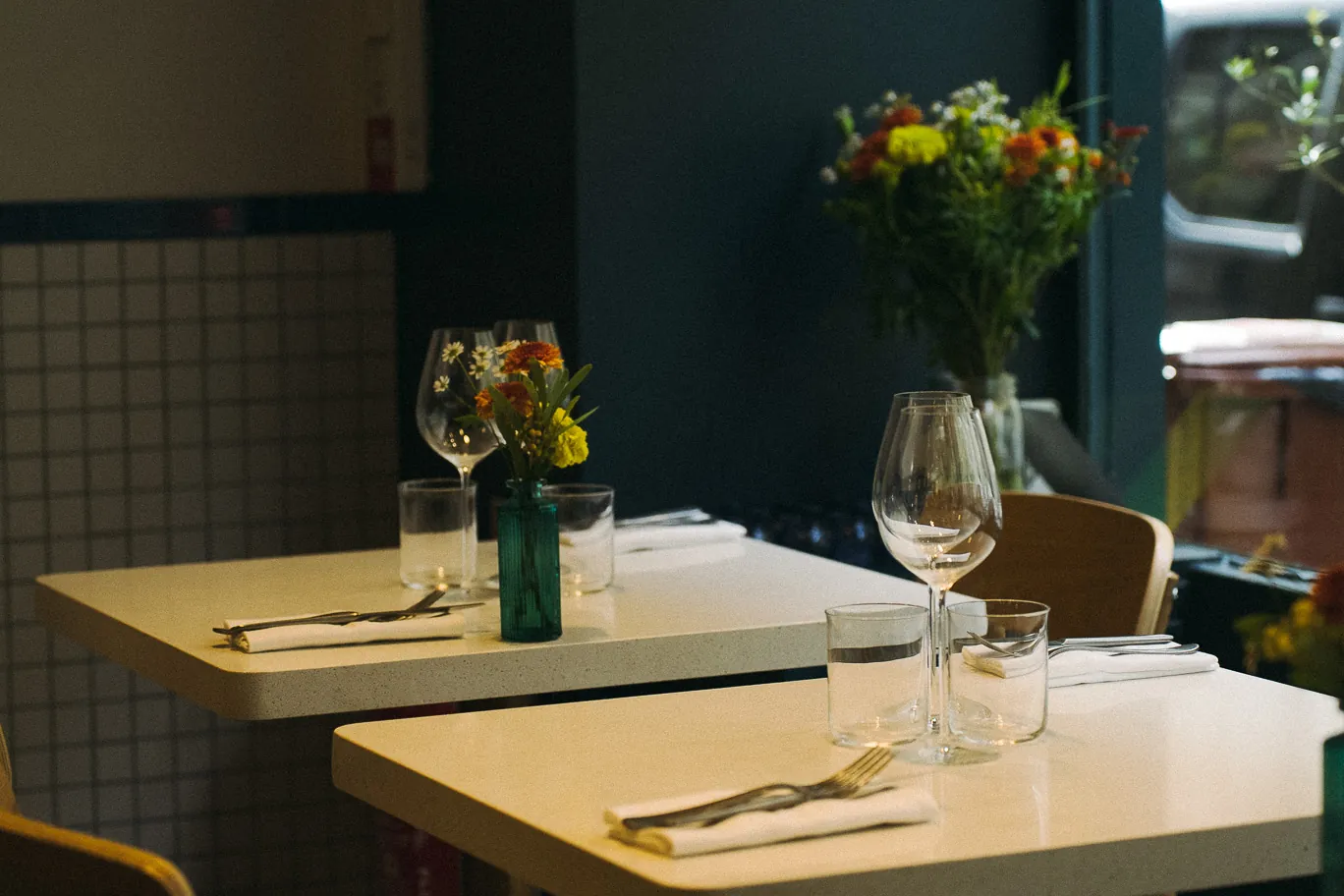 La salle de Barbo, tables dressées : verres à vin, couverts et petits bouquets de fleurs.